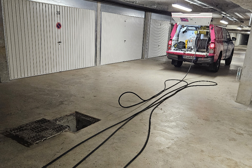 Intervention de débouchage de canalisation dans les garages d'un immeuble dans l'Aude. Pick-up en place dans le garage sous-terrain avec tuyau pour l'hydrocurage sorti