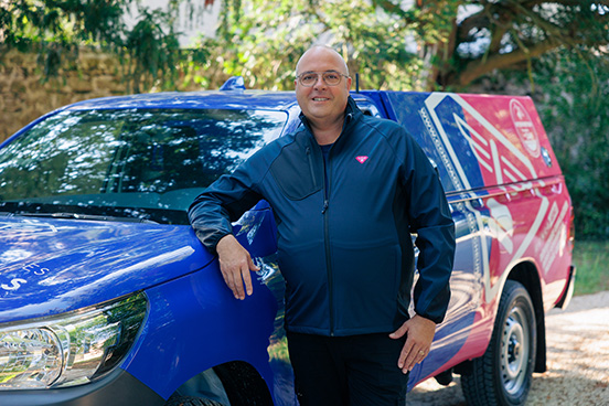 Photo de Paulo Teixeira, déboucheur dans le département du Bas-Rhin, accoudé à son pick-up d'intervention  rose et bleu